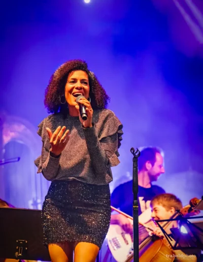 Jammin’Cool Sängerin Caroline Mhlanga singt gestikulierend im blau-violetten Bühnenlicht