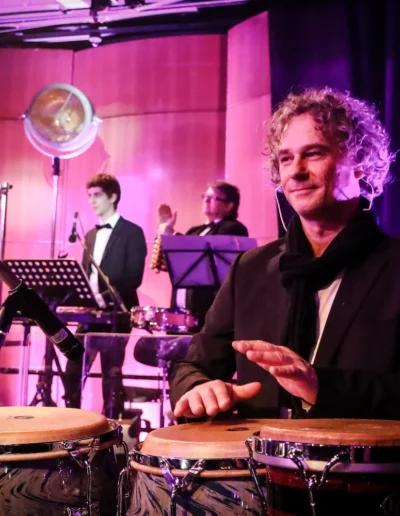 Mark Collazo, Percussionist bei Jammin’Cool, lächelnd im pinken Bühnenlicht
